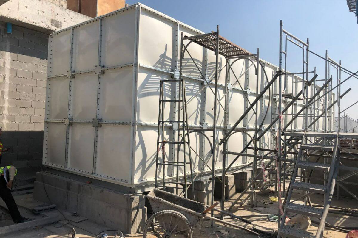 Large rectangular modular water storage tank being assembled on a concrete base with scaffolding and ladders around it