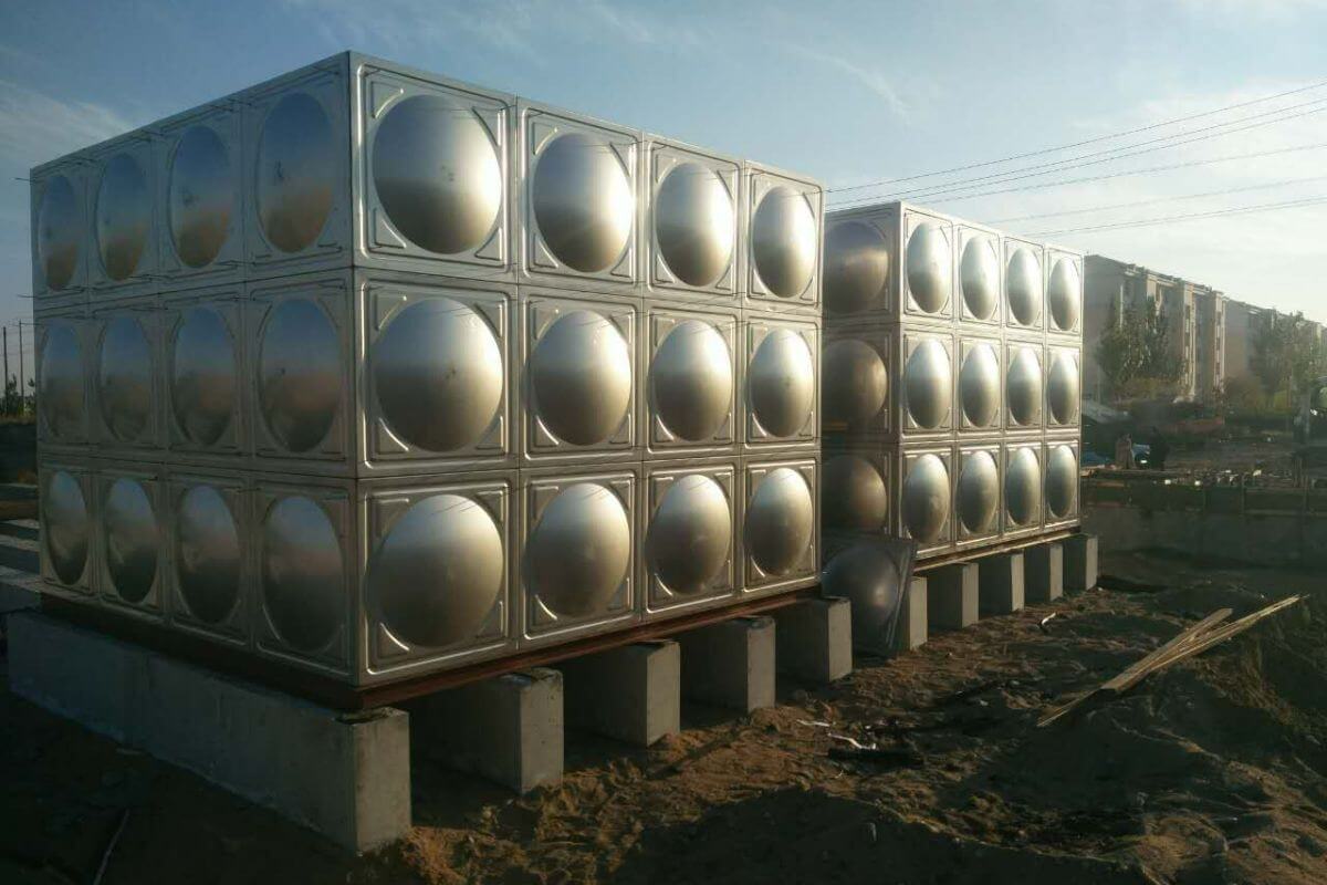 Two stainless steel modular water storage tanks installed outdoors on concrete supports at a construction site