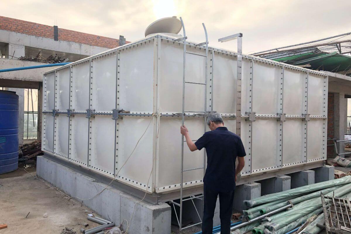 Man inspecting a large white modular commercial water tank with a ladder at a construction site