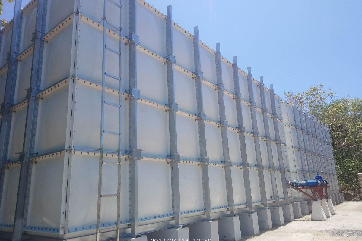 Outdoor white modular water storage tank installed on concrete supports with a ladder and blue piping