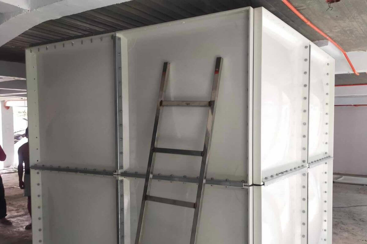 White modular water storage tank installed under a building with a ladder leaning against it