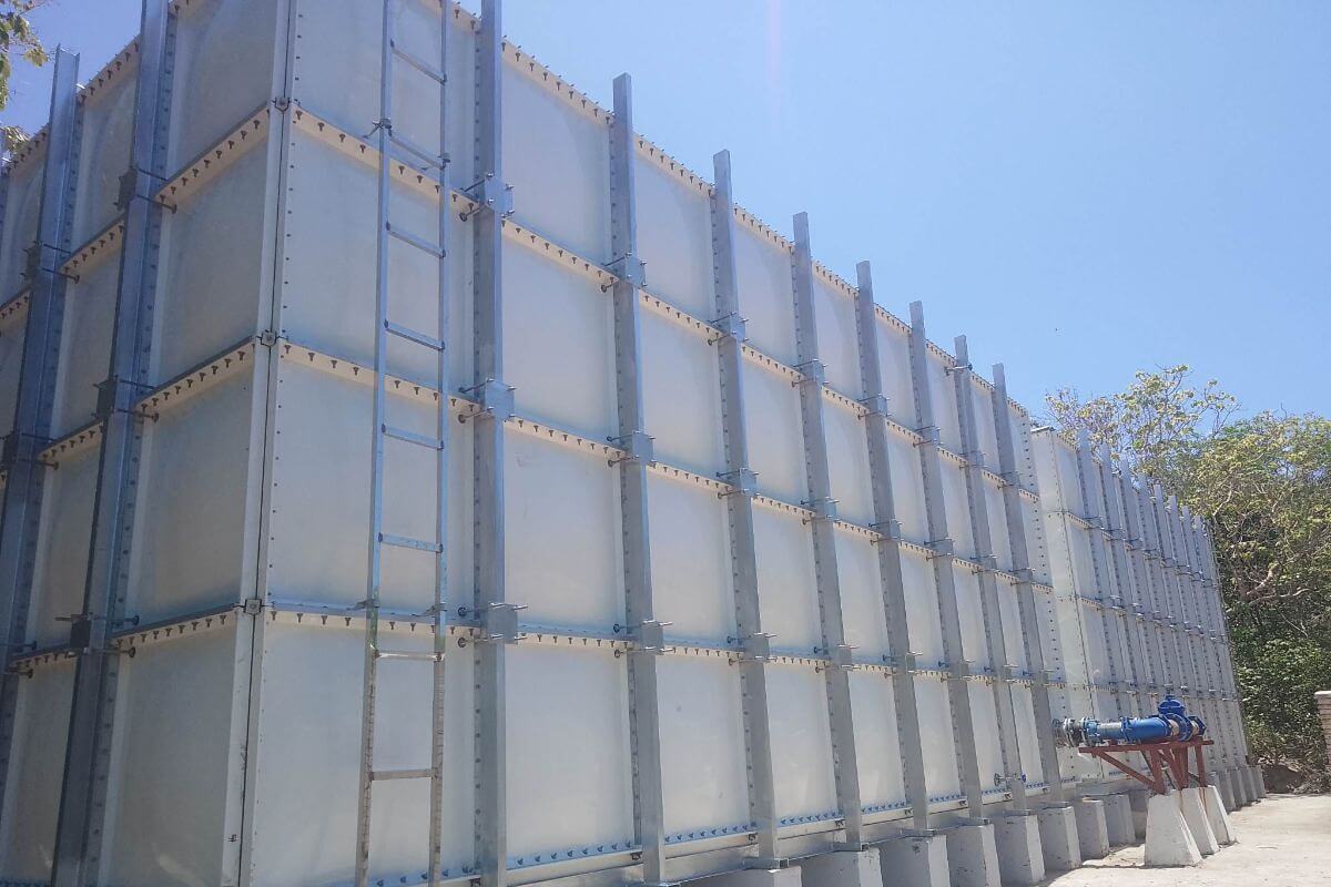 Low-angle exterior view of a tall, multi-panel FRP sectional water storage tank under a clear sky