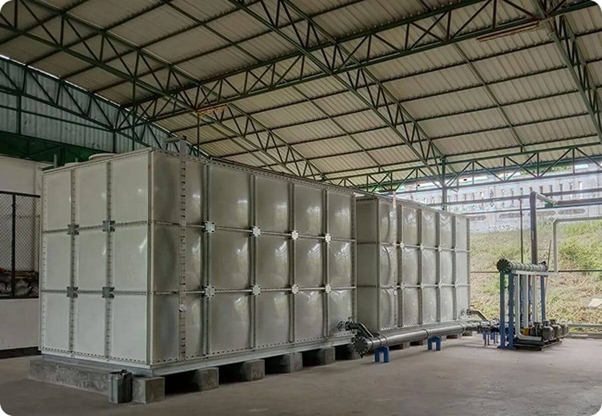Large white indoor sectional GRP water storage tank installed inside an industrial warehouse facility