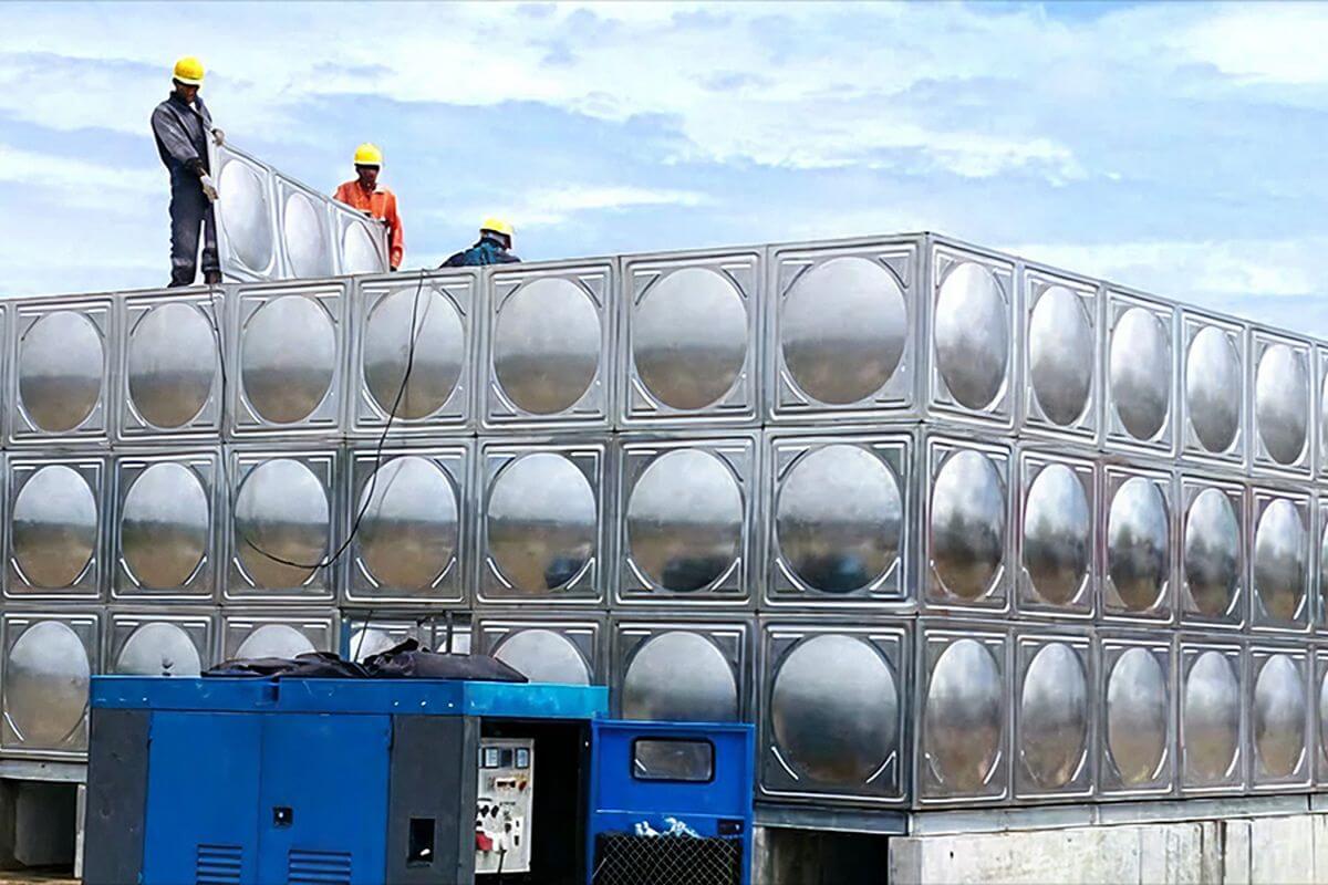 Construction workers installing stainless steel pressed panels on top of a large modular water tank system.