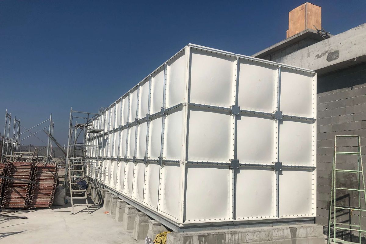 Newly installed white sectional FRP water storage tank on a concrete foundation during a commercial construction project.