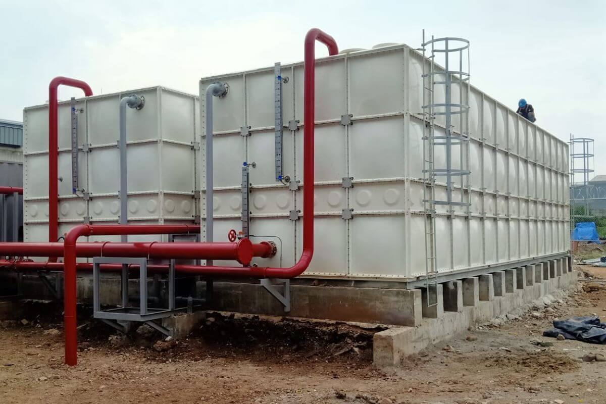 Outdoor modular FRP sectional water tank with integrated red piping and maintenance access ladder.